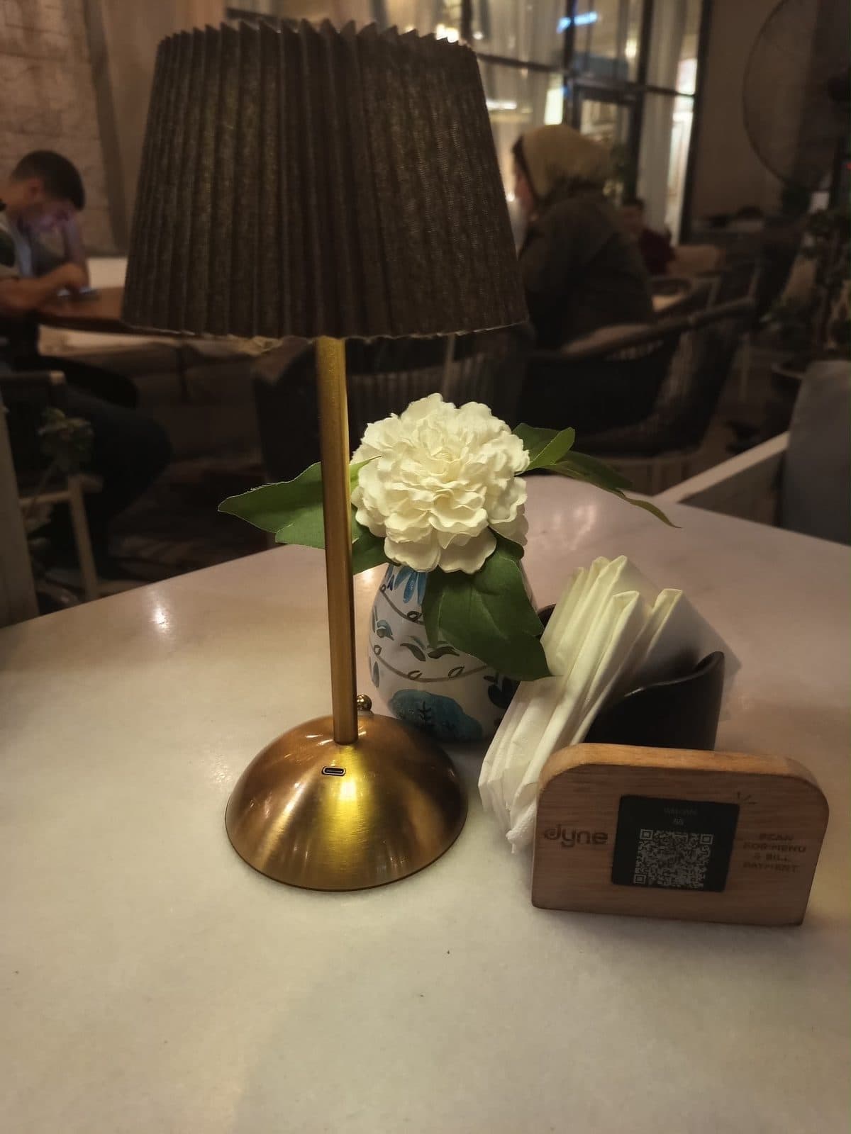 A laid table inside Willow's Arkan Plaza, with a table lamp and a small vase of flowers.