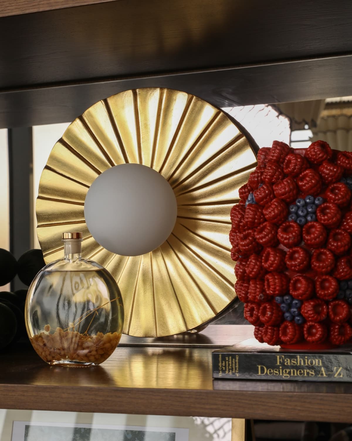 A styling detail at Willow's Golf Central: a pleated gold wall light beside a glass bottle of dried grasses on a dark wood shelf.